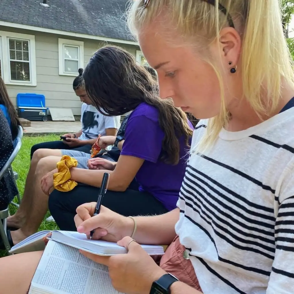 Girl writing in journal over Bible in lap.