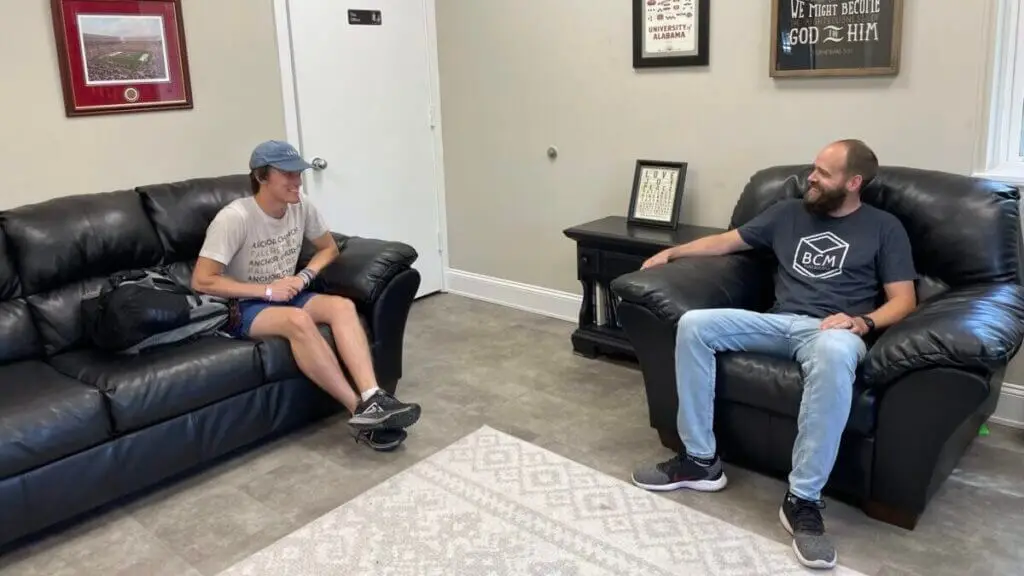 College student sits on couch talking to his ministry mentor seated in a large chair