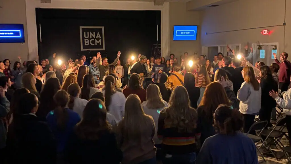 Large group of college students gather around worship band for worship service